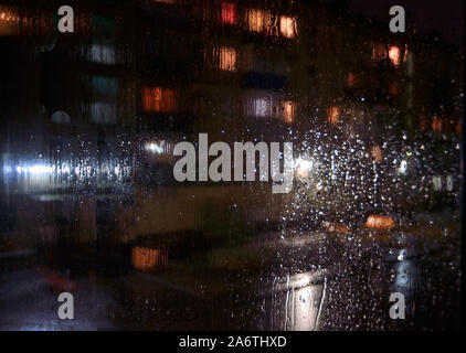 Sityscape pluvieux nuit à l'extérieur de la fenêtre - volet arrière-plan flou flou artistique avec des gouttes d'eau sur le verre, de l'éclairage de nuit, flou des voitures en stationnement. Mela Banque D'Images