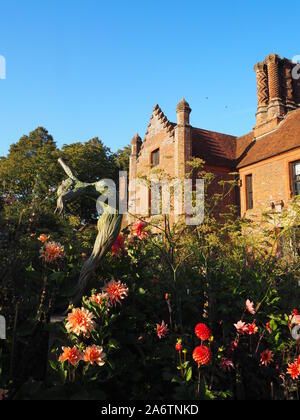 Chenies Manoir et jardin à la fin de l'été dans une belle soirée. rose lumineux dahlia variétés, ciel bleu, grands arbres encadrent.Une sculpture atteint le haut. Banque D'Images