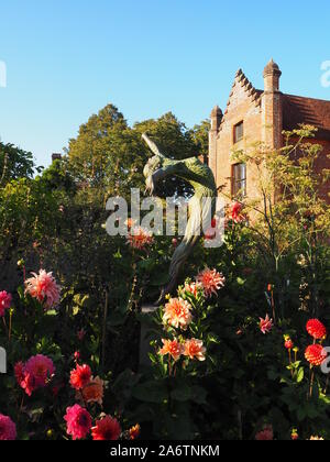 Chenies Manoir et jardin à la fin de l'été dans une belle soirée. rose lumineux dahlia variétés, ciel bleu, grands arbres encadrent.Une sculpture atteint le haut. Banque D'Images