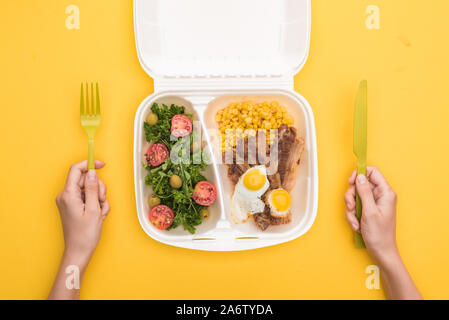 Portrait de femme tenant un couteau, fourchette en plastique et eco emballage avec le maïs, la viande, œufs frits et salade jaune isolé sur Banque D'Images