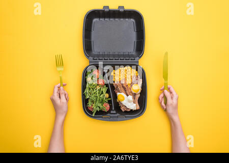 Portrait de femme tenant un couteau, fourchette en plastique et eco emballage avec le maïs, la viande, œufs frits et salade jaune isolé sur Banque D'Images