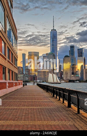 Navigation le long de la skyline de NEW YORK - Un voilier voyages sur le fleuve Hudson le long du bas du New York City pendant le coucher du soleil. Les reflets dorés du soleil sont refléter Banque D'Images