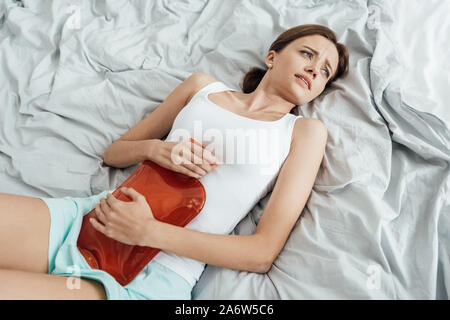 Vue aérienne de la souffrance young woman Lying in Bed and holding plus chaude Banque D'Images