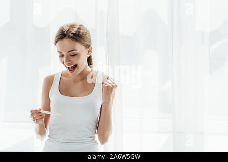 Jeune femme montrant test de grossesse et oui à la maison des gestes Banque D'Images