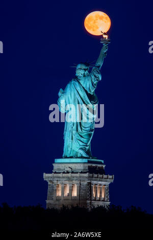 La super pleine lune se lève au-dessus de la Statue de la liberté au cours de l'heure bleue la pleine lune s'aligne parfaitement avec les statues chalumeau. Banque D'Images