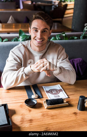 Heureux homme assis à table près de sushi bar avec menu Banque D'Images