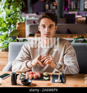 Bel homme assis dans les sushi bar près de délicieux repas Banque D'Images