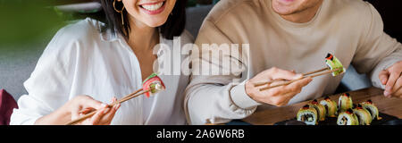 Vue panoramique tourné de happy man and woman holding baguettes avec de délicieux sushis dans un restaurant Banque D'Images