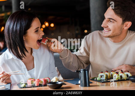 Focus sélectif de happy man holding baguettes avec de délicieux sushi près de young woman in restaurant Banque D'Images