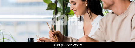 Vue panoramique tourné de young man holding chopsticks près de happy woman in sushi bar Banque D'Images