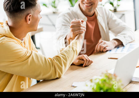 Portrait de deux jeunes hommes d'une poignée de main tout en étant assis ensemble au lieu de travail Banque D'Images