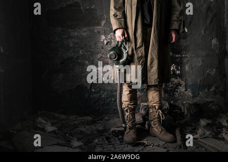 Portrait d'homme tenant un masque à gaz en position debout près du vieux mur dans la chambre abandonnée, concept post apocalyptique Banque D'Images