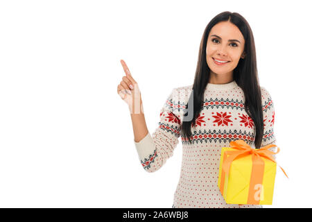 Cheerful woman in sweater holding present et en pointant avec le doigt isolated on white Banque D'Images