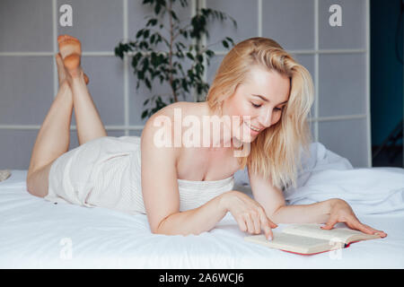 Belle femme blonde lit un livre dans le lit dans la chambre à coucher Banque D'Images