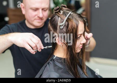 Coiffeur professionnel coupe les cheveux bruns de la femme en instituts de beauté. Banque D'Images