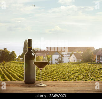 Verre et bouteille de vin en bois avec rampe sur scène rurale du pays en arrière-plan. Feuilles vert et calme le soleil d'été 24. Copyspace. Des boissons d'alcool sur l'arrière-cour de grande maison. Banque D'Images