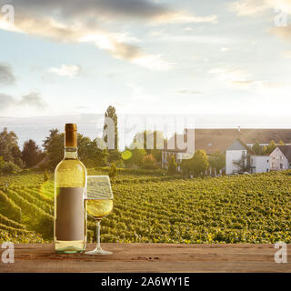 Verre et bouteille de vin en bois avec rampe sur scène rurale du pays en arrière-plan. Feuilles vert et calme le soleil d'été 24. Copyspace. Des boissons d'alcool sur l'arrière-cour de grande maison. Banque D'Images