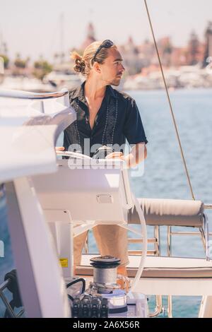 Tir vertical d'un homme blond marin sur un blanc bateau regardant la belle mer Banque D'Images