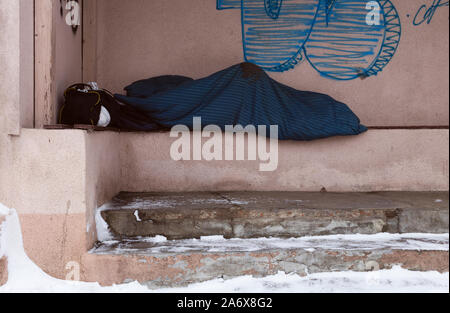 Sans-abri dormir sur la station de bus. Ses chaussures couché à côté de lui. Banque D'Images