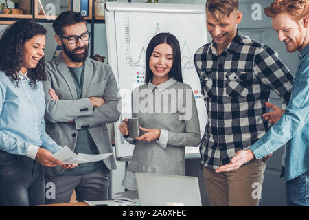 Startupers travailler ensemble au comité permanent du bureau à l'écran du portable au joyeux sourire Banque D'Images
