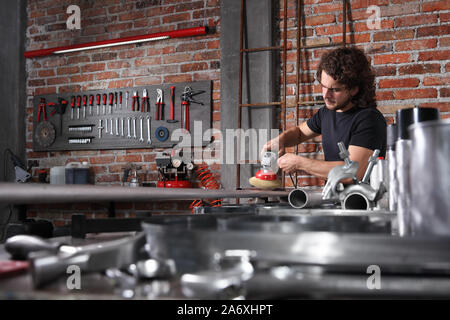 L'homme à l'atelier de maison travail garage metal avec brosse d'angle meuleuse, réparer la machine, les brosses de nettoyage et la pipe du fer sur l'établi plein de clés dynamométriques Banque D'Images