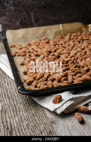 Amandes brûlées étendu sur la lèchefrite, noir, papier chiffon blanc rustique en bois texturé sur table, trois amandes brûlées en premier plan de pose Banque D'Images