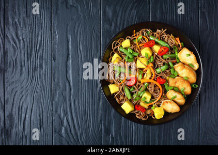 La mangue Poulet et nouilles soba avec salade de haricots verts cuits à la vapeur, carottes râpées, les poivrons et oignons de printemps dans un bol noir sur une table en bois, vie Banque D'Images