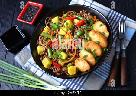 La mangue Poulet et nouilles soba avec salade de haricots verts cuits à la vapeur, carottes râpées, les poivrons et oignons de printemps dans un bol noir sur une table en bois, vie Banque D'Images