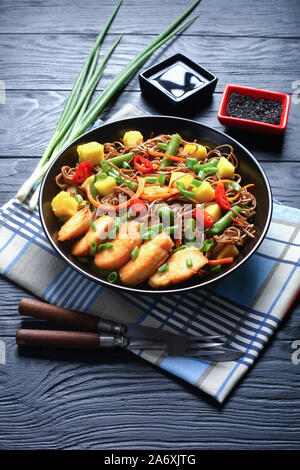 La mangue Poulet et nouilles soba avec salade de haricots verts cuits à la vapeur, carottes râpées, les poivrons et oignons de printemps dans un bol noir sur une table en bois, ver Banque D'Images