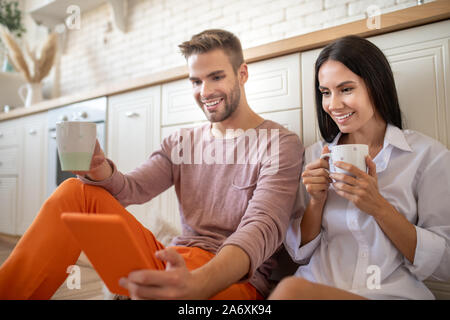 Smiling couple regardant la vidéo sur tablette et de boire du café Banque D'Images