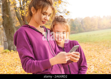 Loisirs de plein air. Une sœur à l'aide de l'app sur smartphone curieux tandis qu'un autre à l'écran au comité permanent dans le parc close-up Banque D'Images