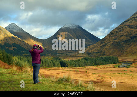 Woman taking photograph on cellphone in Glen Etive, les Highlands écossais. Vue imprenable sur la montagne et la vallée de l'arrière-plan. Banque D'Images