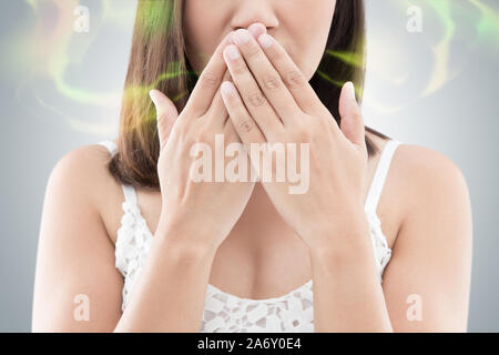 Asian Woman in white porter fermer sa bouche contre la mauvaise haleine, fond gris Banque D'Images