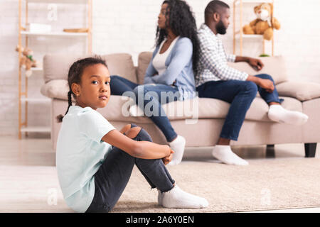 Contrarié black girl sitting séparément des parents après leurs disputes Banque D'Images