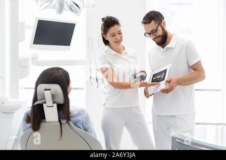 Deux dentistes gaie expliquant le traitement des maladies des dents au patient Banque D'Images