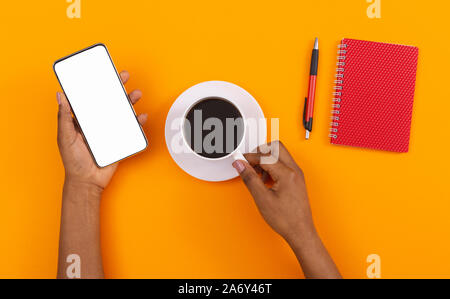 Femme Afro en utilisant Smartphone avec écran blanc et de boire du café Banque D'Images