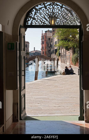 Un couple parler sur un canal tranquille rue que vu de la porte d'Palazzoo Cini, un petit musée à Venise en Italie. Banque D'Images