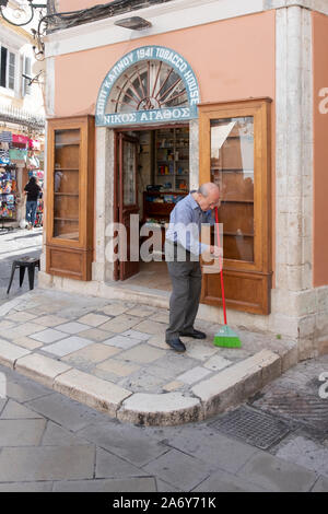 Un ancien commerçant balaie le trottoir à l'extérieur de son bureau de tabac. À Corfou, Grèce. Banque D'Images