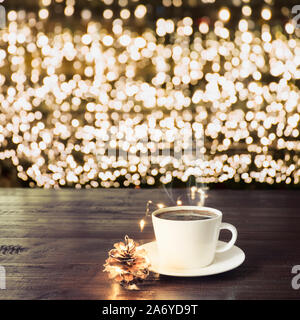 Tasse de café noir et de décor sur planche de bois dans le café. Or floue garland comme arrière-plan. Le temps de Noël. Motif de Noël Banque D'Images
