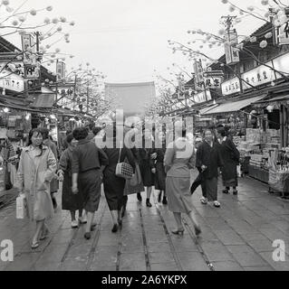 Années 1960, historique, déjeuner et un groupe de jeunes femmes japonaises travaillant marchant le long d'une rue de marché en plein air à Tokyo, Japon. Banque D'Images