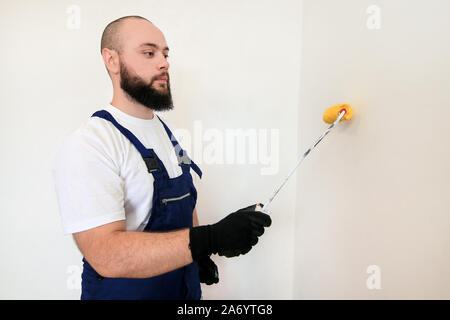 Travailleur de la construction et l'homme à faire terminer la rénovation à l'appartement. À l'aide de rouleau à peindre peintre peinture brosse de mur avec la couleur jaune. Banque D'Images