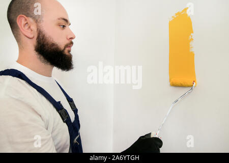 Travailleur de la construction et l'homme à faire terminer la rénovation à l'appartement. À l'aide de rouleau à peindre peintre peinture brosse de mur avec la couleur jaune. Banque D'Images