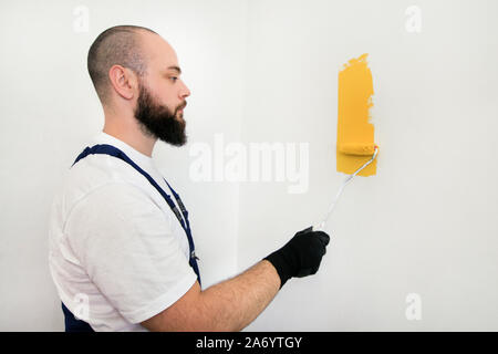 Travailleur de la construction et l'homme à faire terminer la rénovation à l'appartement. À l'aide de rouleau à peindre peintre peinture brosse de mur avec la couleur jaune. Banque D'Images