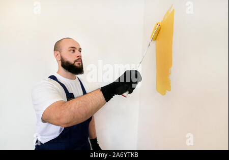 Travailleur de la construction et l'homme à faire terminer la rénovation à l'appartement. À l'aide de rouleau à peindre peintre peinture brosse de mur avec la couleur jaune. Banque D'Images