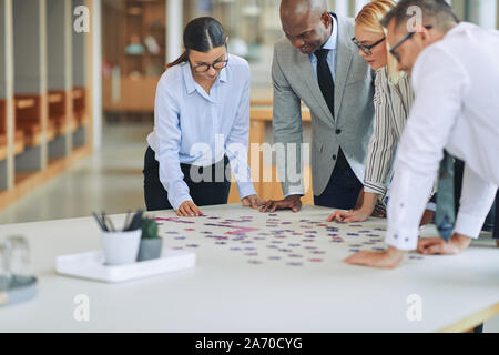 Groupe d'affaires diversifié se tenant ensemble autour d'une table de conférence dans un bureau a porté sur d'essayer de résoudre un puzzle Banque D'Images