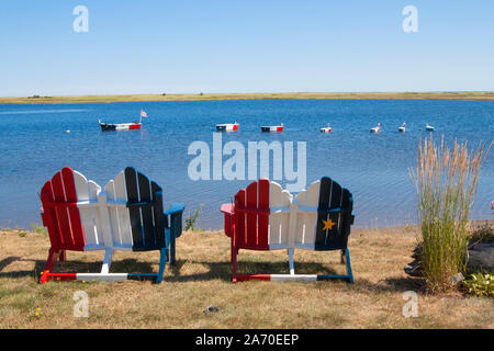 Chaises en bois le long de la côte et des décorations en bateau sur l'eau peint aux couleurs des Français drapeau acadien sur la côte près de Bouctouche Nouveau Brun Banque D'Images