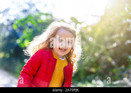 Adorable petite fille qui marche dans la région de park sur un jour d'automne. Female toddler de jaune, rouge et mauve les vêtements. Banque D'Images