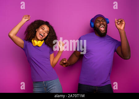 Couple avec casque d'écoute de la musique et de la danse avec énergie sur fond violet Banque D'Images