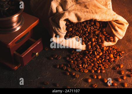 Ancien moulin à café et grains de café dispersés dans un sac sur un fond en béton. Banque D'Images