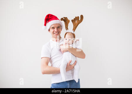 Mon premier Noël. Papa in santa hat holding sa fille bébé fille portant des cornes de cerf en sur fond blanc avec copie espace Banque D'Images